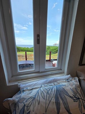 A window with a view of a grassy area and a building in the distance. - Bluecove Hideaway Relaxing Retreat - Guarida Azul 3BR  Private Pool + Ocean View (Quebradillas)