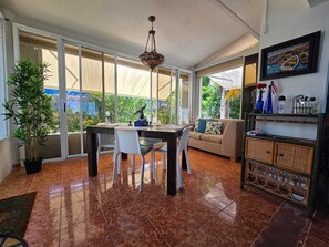 A spacious room with a dining table, chairs, a sofa, a chandelier, and a view through large windows. - Bluecove Hideaway Relaxing Retreat - Guarida Azul 3BR  Private Pool + Ocean View (Quebradillas)