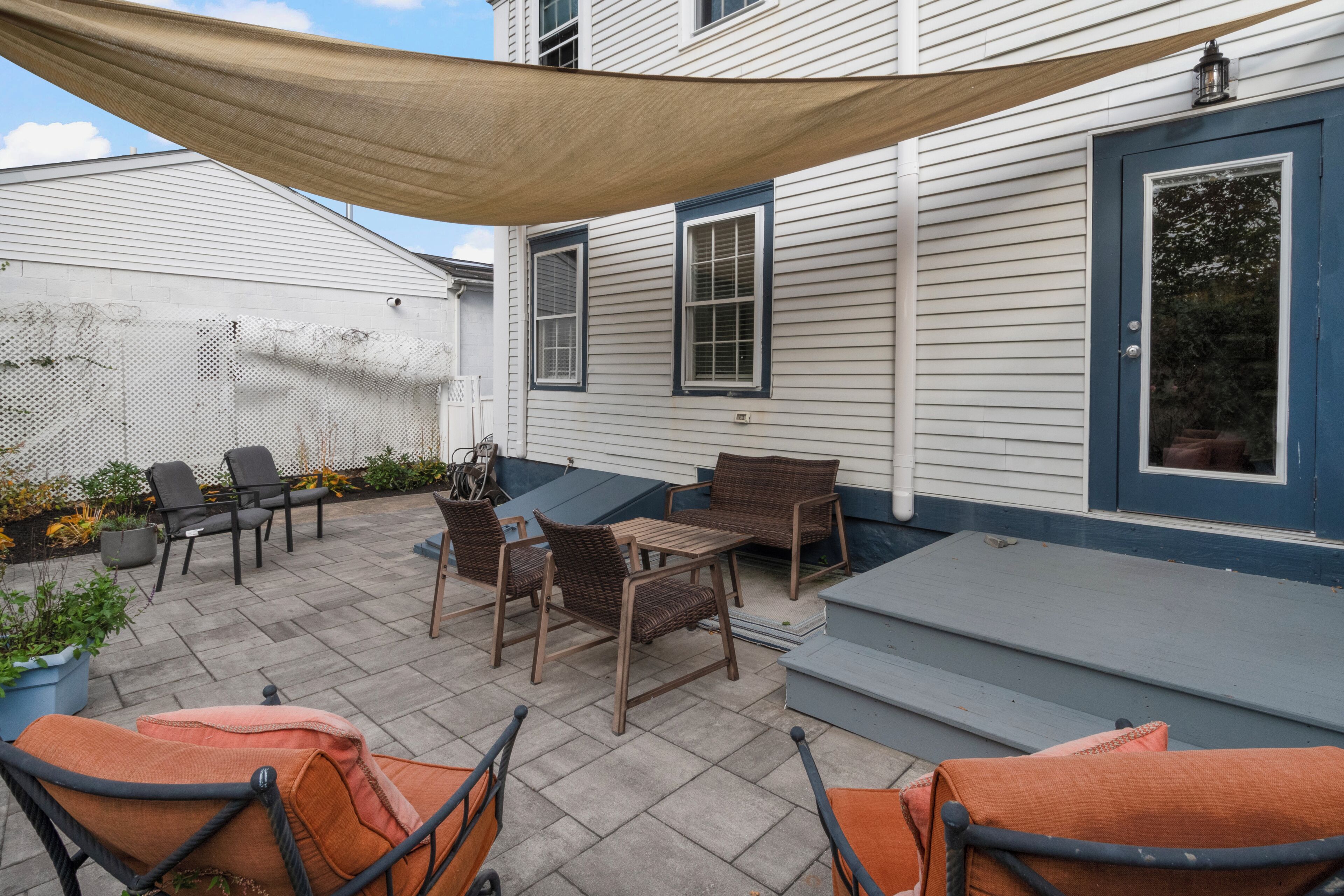 A patio with outdoor furniture, a shaded area, and a house with a blue door.