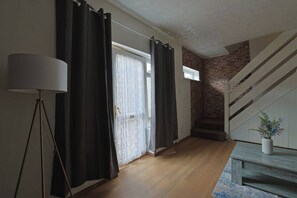 Ein Zimmer mit Holzboden, einer Wendeltreppe an einer Ziegelwand und einer Tür mit Vorhängen.