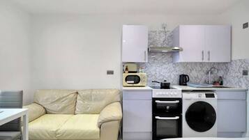A compact kitchenette with a sofa, a microwave, a stove, a washing machine, and a small table.