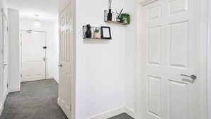 Un pasillo con puertas blancas, una lámpara y una estantería con adornos.