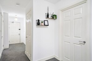 Um corredor com portas brancas, um candeeiro e uma prateleira com objetos decorativos.