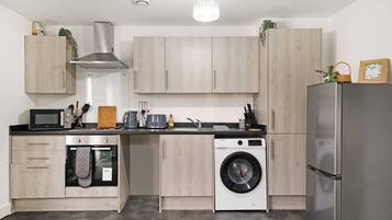 A compact kitchen with a microwave, kettle, sink, and washing machine.
