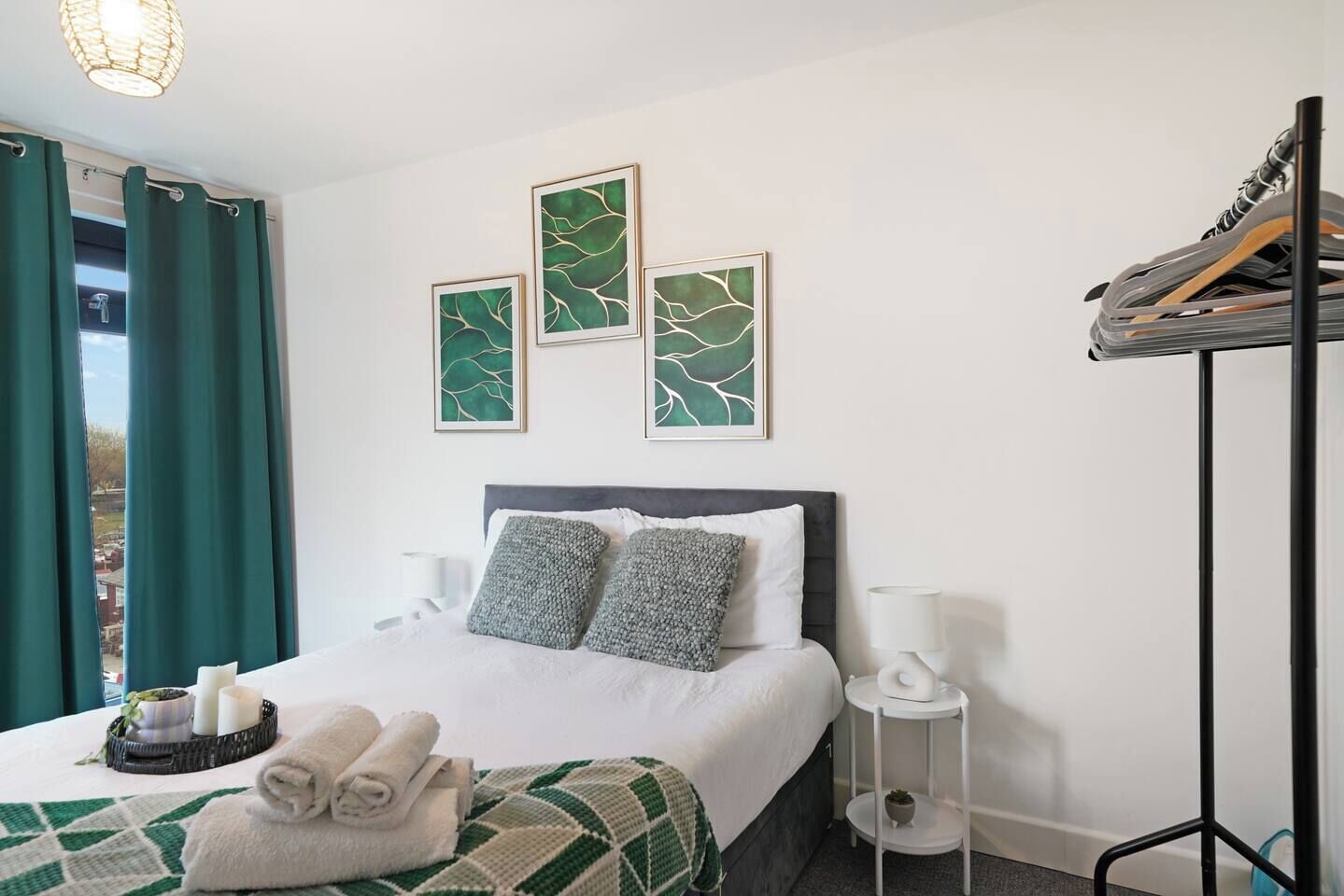 A hotel room with a bed, pillows, a bedside table, a lamp, a wall-mounted shelf, and a window with curtains.
