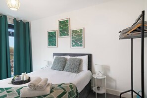 Ein Hotelzimmer mit einem Bett, Kissen, einem Nachttisch, einer Lampe, einem Wandregal und einem Fenster mit Vorhängen.