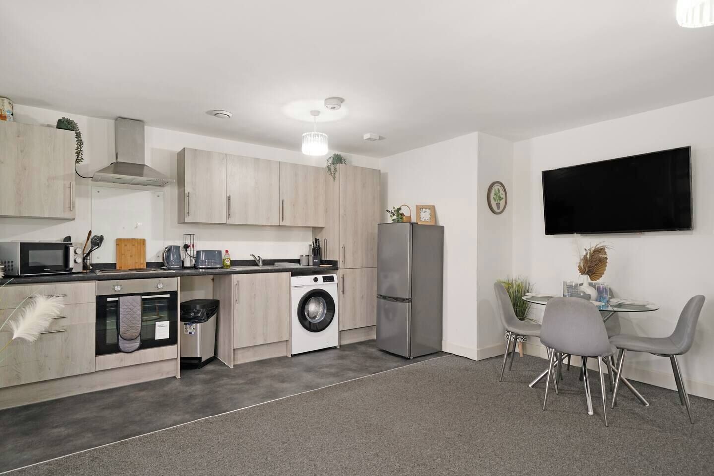 Cozinha compacta com micro-ondas, forno, máquina de lavar e frigorífico. Dispõe de zona de refeições com mesa e cadeiras.