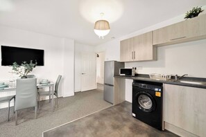 A compact kitchen with a washing machine, a microwave, and a dining area with a table and chairs. - Heathrow Gateway Apartments with Private Parking17 (Colnbrook)