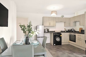 A modern kitchen with a built-in washing machine, a dining area with a table set for two, and a small plant on the counter.