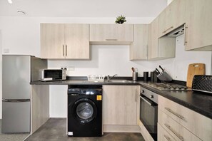 A modern kitchen with a built-in washing machine, a microwave, and a sink. - Heathrow Gateway Apartments with Private Parking17 (Colnbrook)
