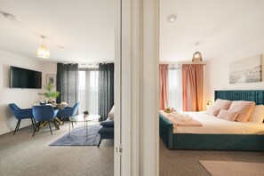 A hotel room with a bed, a desk, chairs, a TV, and a plant. - Heathrow Gateway Apartments with Private Parking35 (Colnbrook)