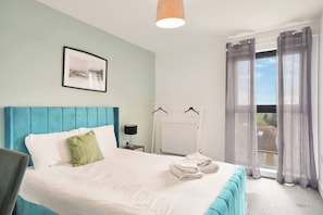 A bedroom with a bed, a bedside table, a radiator, and a window with curtains.