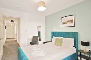Une chambre d’hôtel avec un lit, un bureau, une chaise, un miroir et un tableau au mur.