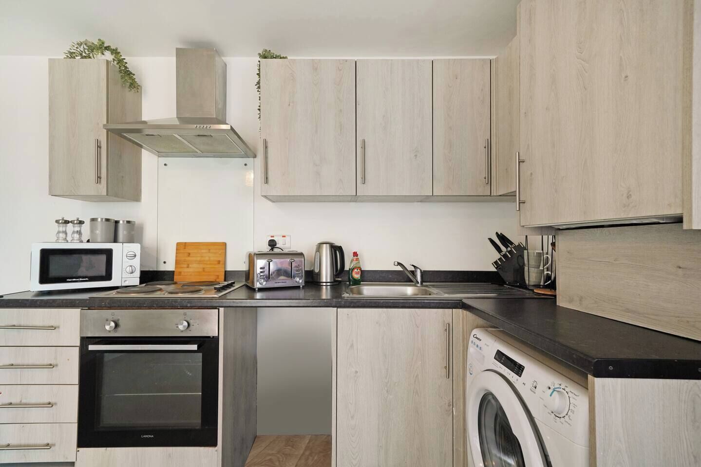 A modern kitchen with stainless steel appliances, wooden cabinets, and a built-in washing machine.