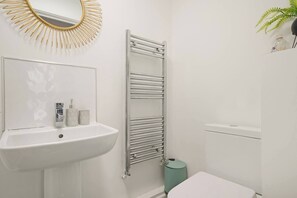 Ein Badezimmer mit einem weißen Waschbecken, einem Spiegel mit Sonnenstrahlrahmen, einem Handtuchhalter und einer Toilette.