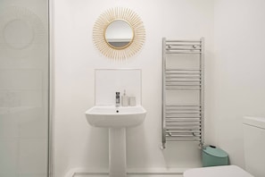 A bathroom with a white sink, a mirror, and a towel rack. - Heathrow Gateway Apartments with Private Parking33 (Colnbrook)