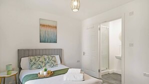 Una camera d'hotel con un letto, un comodino, una lampada, un quadro e una porta che dà su un bagno.