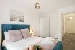 A hotel room with a bed, a wardrobe, a bedside table, and a hanging light fixture. - Heathrow Gateway Apartments with Private Parking35 (Harlington)