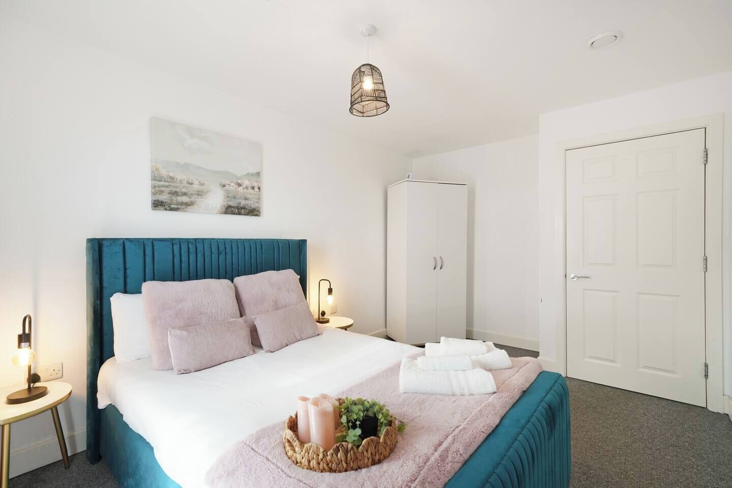 A bedroom with a bed, bedside lamps, a wardrobe, a door, and a hanging light fixture.