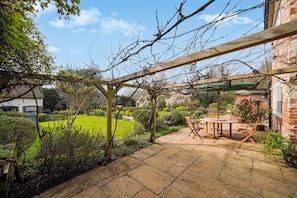 Un patio con una pérgola, una mesa con sillas y un edificio de ladrillo al fondo.
