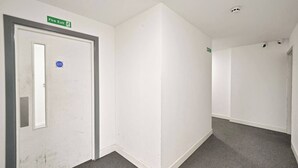 Um corredor com uma porta de saída de incêndio, uma placa indicando saída de incêndio e um detector de fumaça no teto.