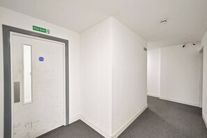 A corridor with a fire exit door, a sign indicating a fire exit, and a smoke detector on the ceiling.
