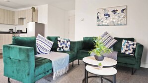 Uma sala de estar com dois sofás verdes, uma mesa de centro e um quadro na parede.