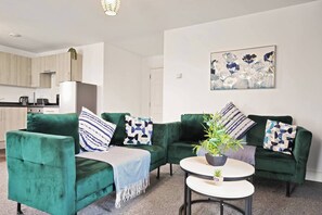A living room with two green sofas, a coffee table, and a painting on the wall.
