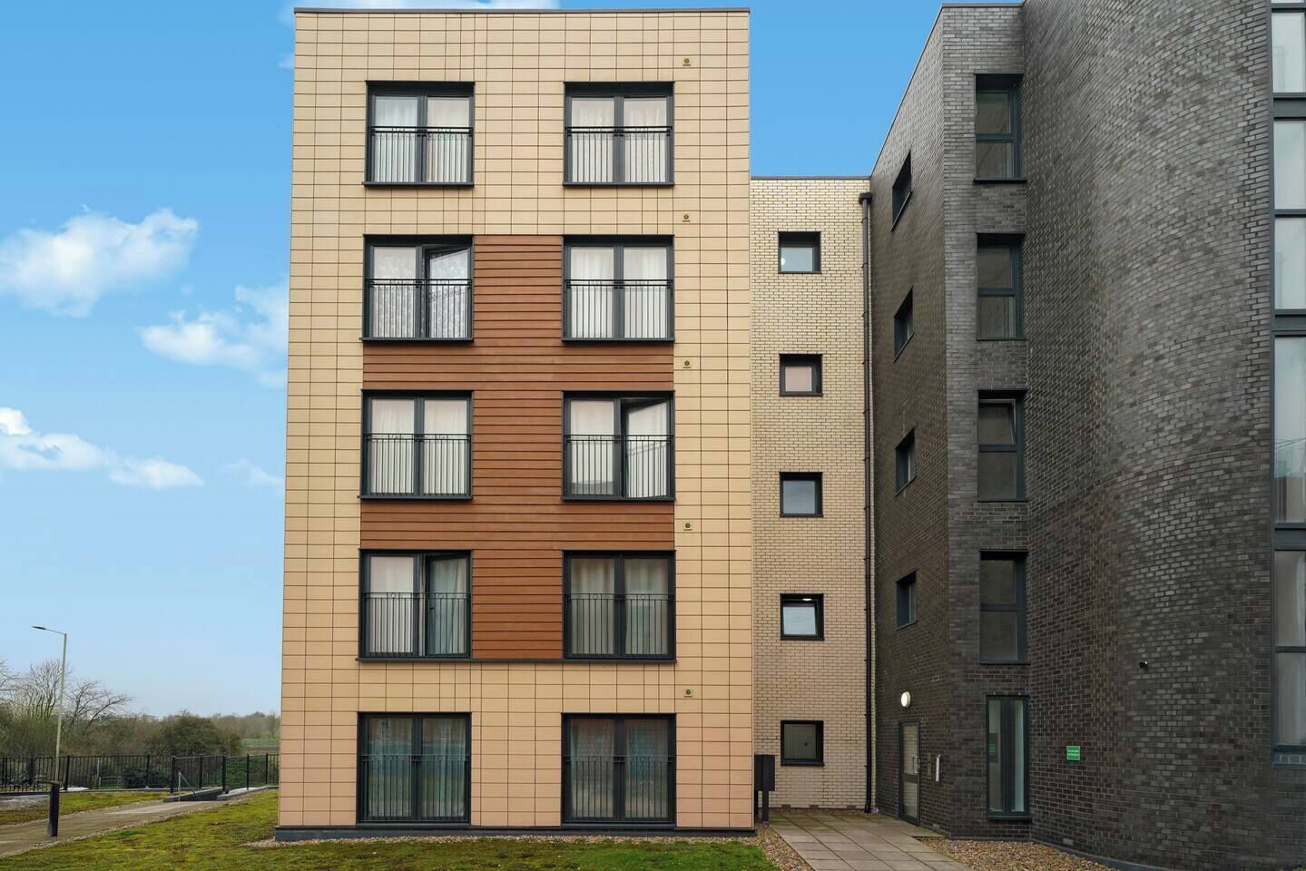 A multi-story residential building with a modern design, featuring a combination of brick and panel facades, large windows, and balconies.