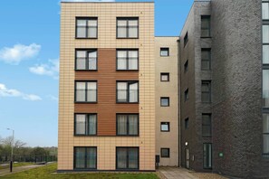 Un immeuble résidentiel à plusieurs étages, doté d’un design moderne, caractérisé par une combinaison de façades en briques et en panneaux, de grandes fenêtres et des balcons.