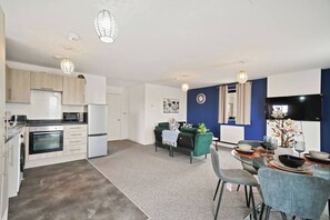 A modern kitchen with built-in appliances, a dining area with a table and chairs, and a living space with a sofa and decorative items. - Heathrow Gateway Apartments with Private Parking13 (London)