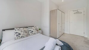A bedroom with a bed, a wardrobe, and a door with a hanger. - Stylish 1BR Near Heathrow & Elizabeth Line 8 (London)