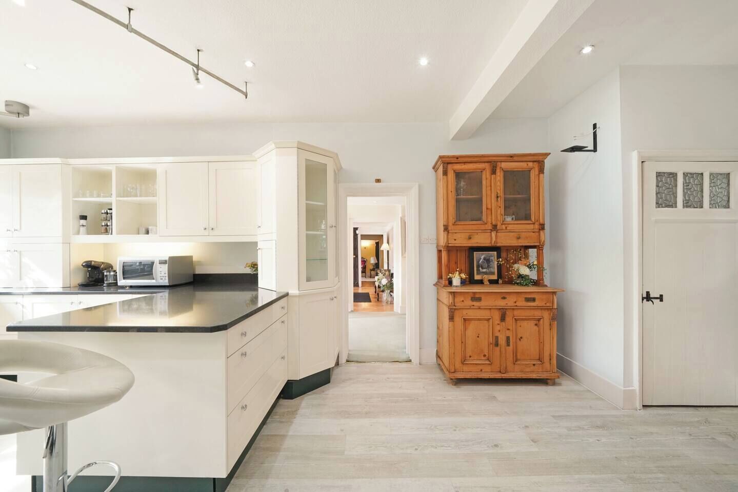 A modern kitchen with white cabinetry, a central island, and a wooden cabinet with glass doors.