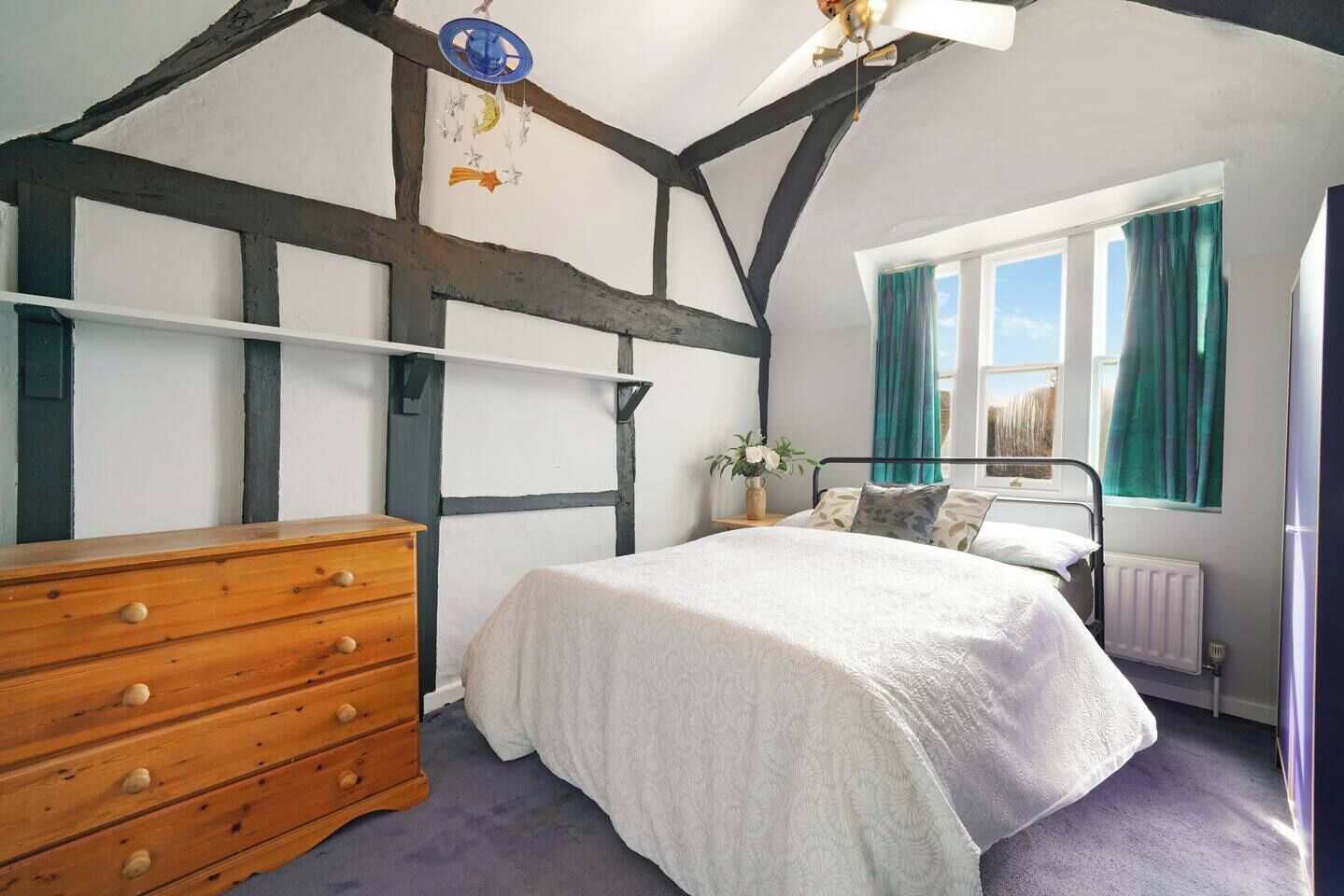 Un dormitorio con cama, cómoda de madera y ventana con cortinas.