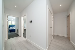 A hallway with a door leading to a bedroom with a blue bed and a bathroom with a shower. - Stylish 2BR Near Heathrow & Elizabeth Line (Harlington)