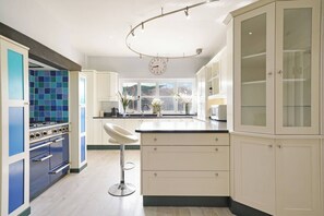 A kitchen with a modern design, featuring a large island, white cabinetry, and a blue-tiled backsplash. - 16th Century manor house | 6BR | Private Grounds (Harlington)