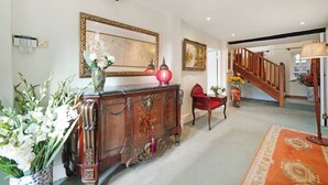 Un hall d’entrée spacieux avec un escalier en bois, un grand miroir et un fauteuil rouge.