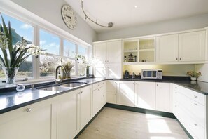 A modern kitchen with white cabinetry, a stainless steel sink, and a window with a view of greenery. - 16th Century manor house | 6BR | Private Grounds (Harlington)