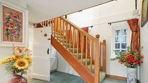Un escalier en bois avec une rampe, un radiateur et un vase rempli de tournesols.