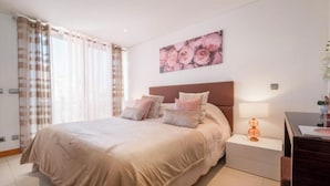 Un dormitorio con una cama grande, una mesita de noche con una lámpara y un cuadro colgado en la pared.