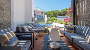 Un área de estar al aire libre con luz solar, piscina, sillones de descanso y una mesa con lámpara.