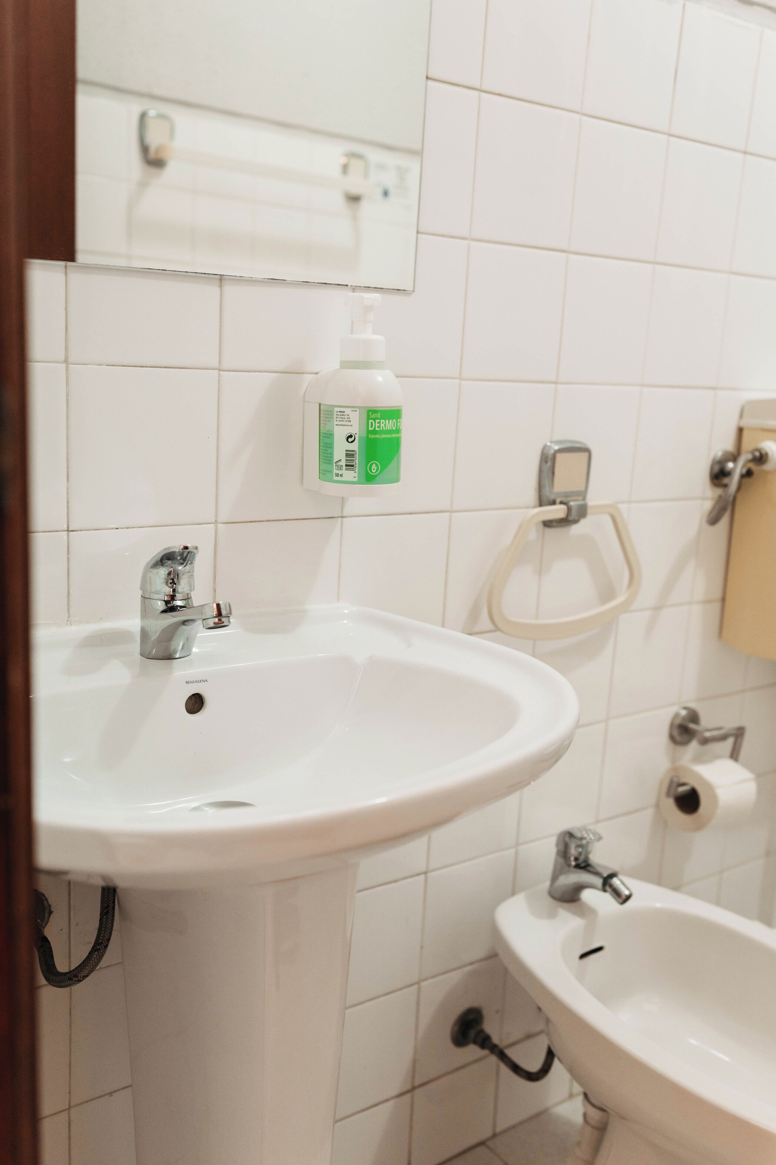 Un baño con lavamanos blanco, espejo e inodoro.