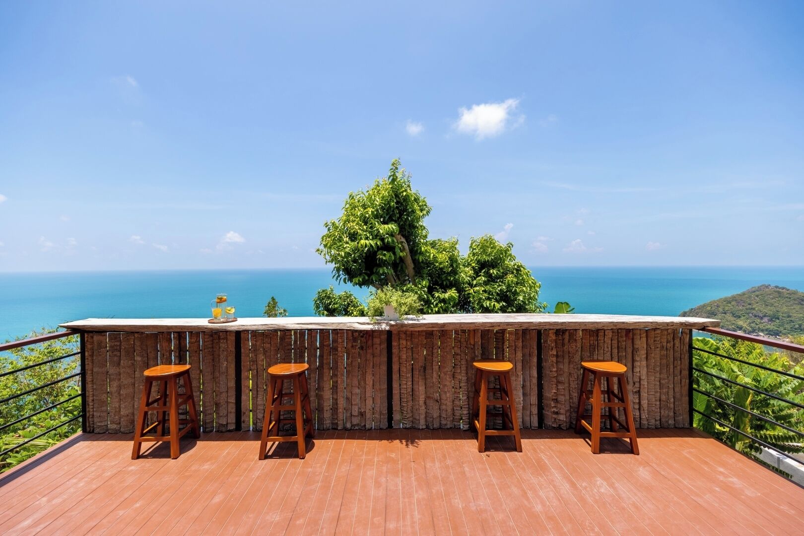 Une terrasse en bois dotée d’un bar et de tabourets, offrant une vue panoramique sur l’océan.