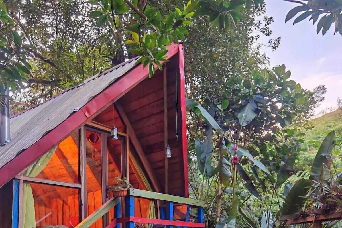 A small, colorful wooden structure with a red roof and blue accents, surrounded by lush greenery and flowering plants.