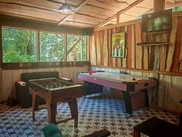 A room with wooden walls, a foosball table, a pool table, and a television.