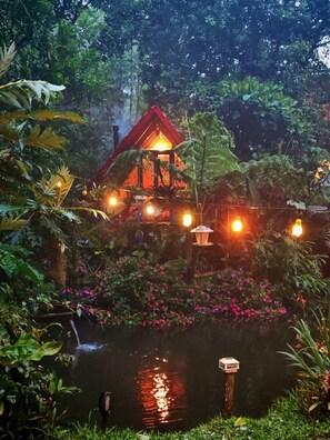 A house with a red roof surrounded by lush greenery and a pond with pink flowers. - DondeLALO Hospedaje (Vara Blanca)