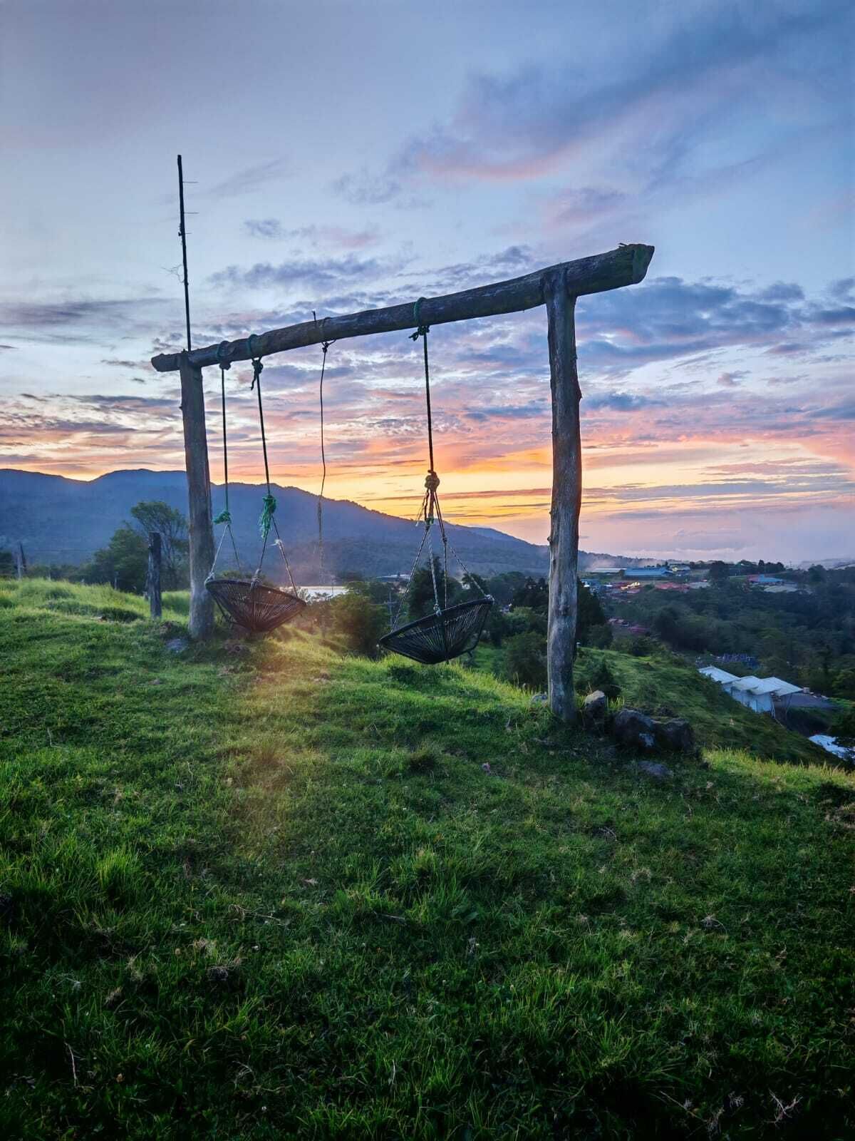 Un columpio de madera en un campo cubierto de hierba, con un atardecer al fondo.