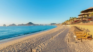 Ein Strand mit einer Reihe von Liegestühlen und Sonnenschirmen, einem klaren, blauen Himmel und ruhiger See.