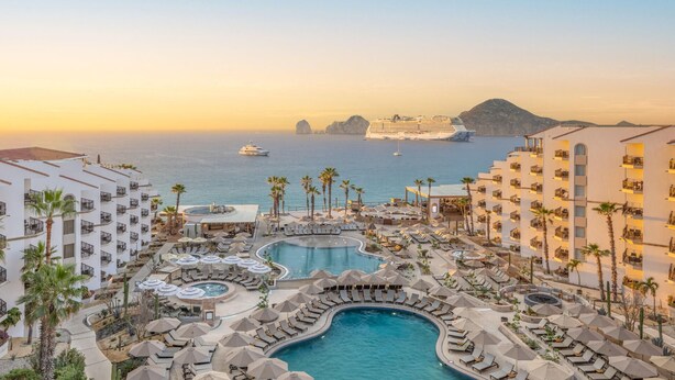 Ein Resort mit mehreren Schwimmbecken, Liegestühlen und Blick auf das Meer und Kreuzfahrtschiffe.
