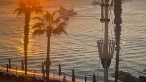 Ein Sonnenuntergangsblick von einer Terrasse am Meer mit Palmen, Liegestühlen und einem Gewässer.